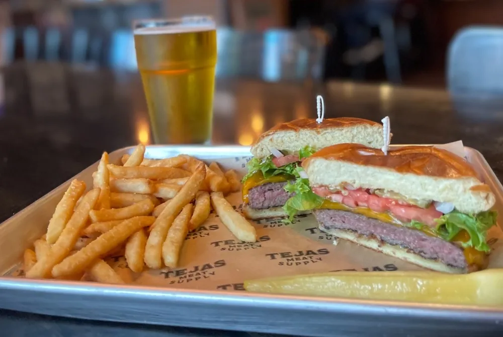 A close-up shot of a single patty burger with melted cheese, lettuce, and tomato, served with a side of crispy fries.