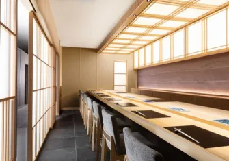 Sushi displayed on a wooden counter with a chef in the background, representing fine dining.