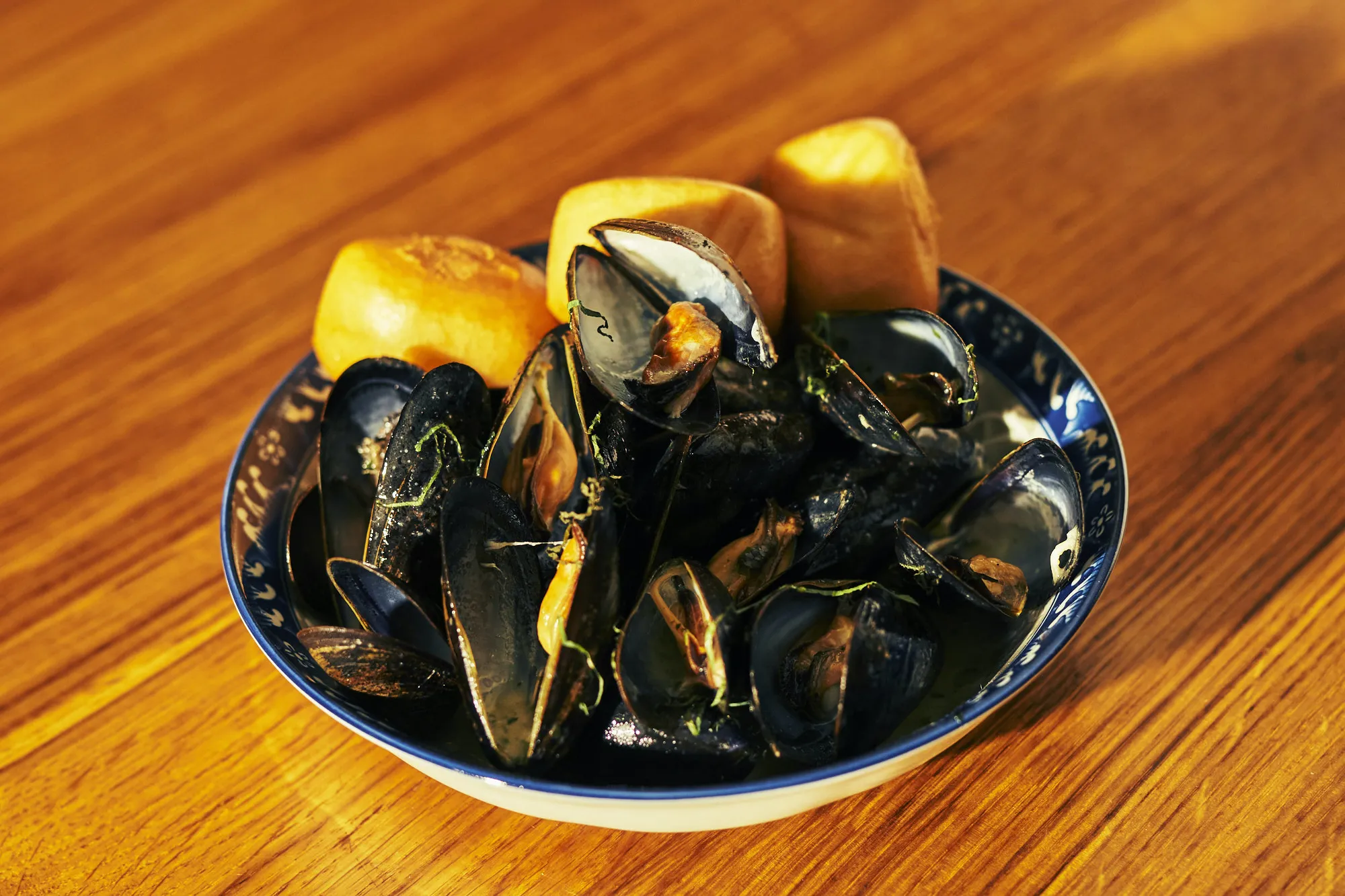 Sake-steamed mussels with mantou buns, an example of a unique Chinese restaurant menu item blending traditional and modern Asian flavors.