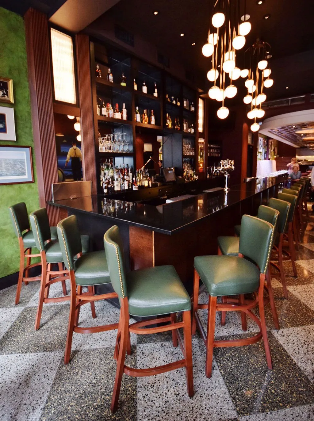 The 20-seat bar area featuring studded green leather barstools and retro lighting fixtures