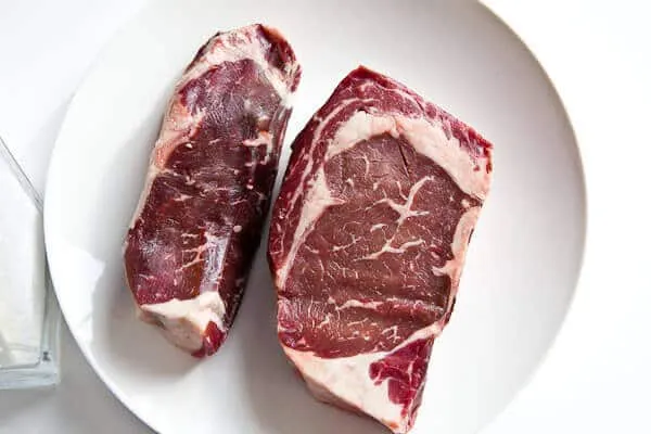 Two thick, raw steaks placed on a surface before salting