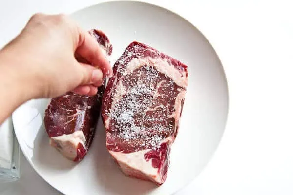 Close-up of a raw steak liberally seasoned with coarse kosher salt