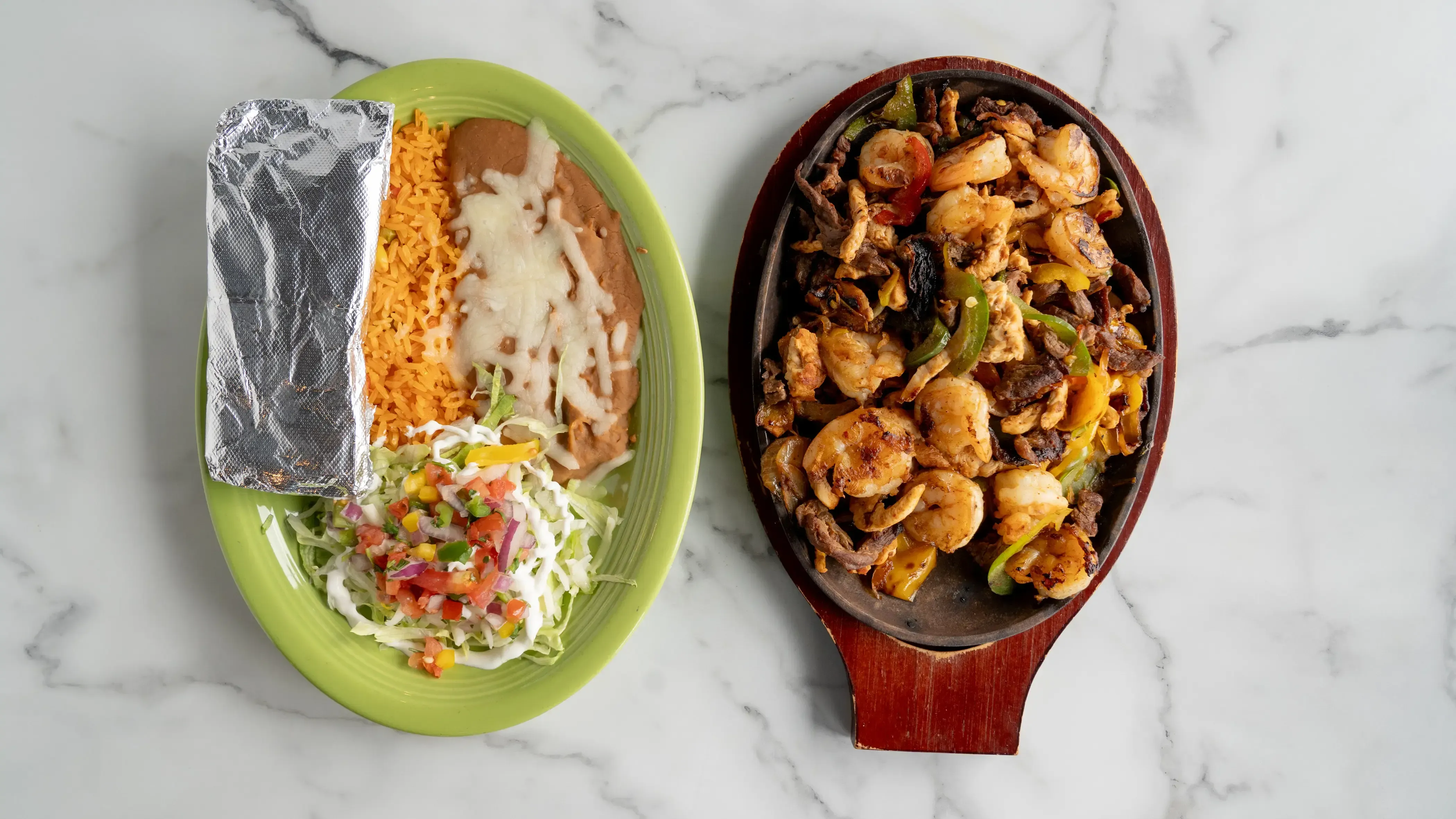 Fajita Texana - Sizzling combination of grilled steak, chicken, and shrimp with bell peppers, onions, and tomatoes. Served with rice, beans, lettuce, sour cream, cheese, pico de gallo, and three tortillas