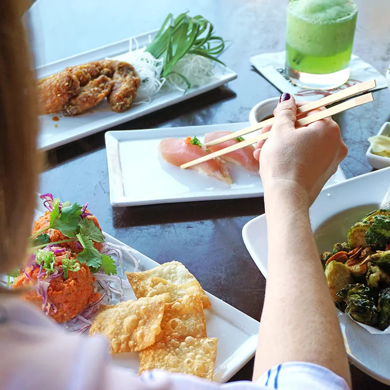 A person sitting at a table with a plate of sushi rolls and small bites, enjoying the Kabuki Happy Hour.