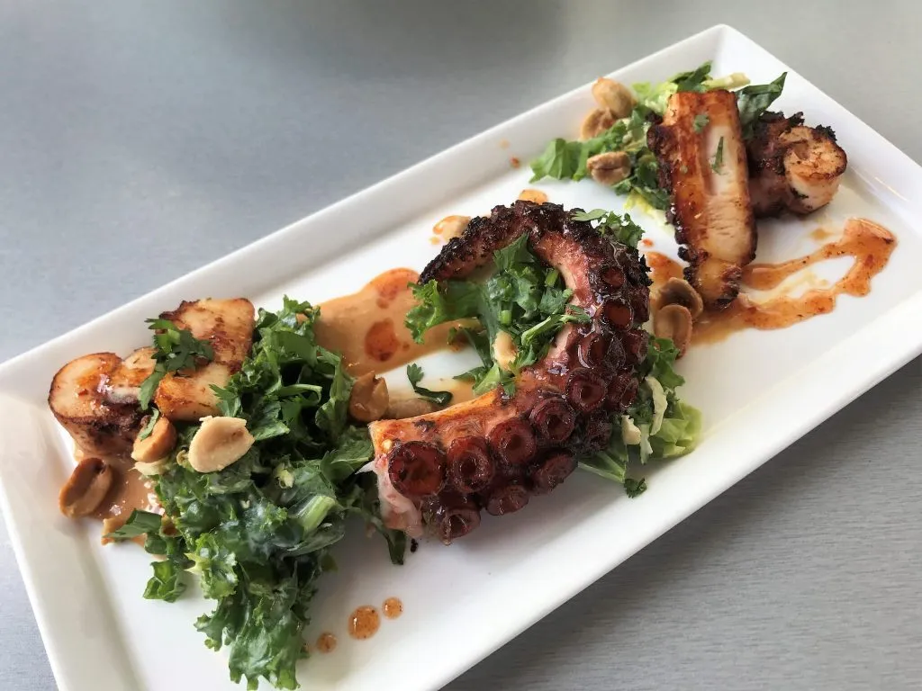 Tender Seared Octopus, artfully arranged with spicy Brussels sprouts, kale slaw, and candied peanuts, a highlight from the moxie's restaurant menu