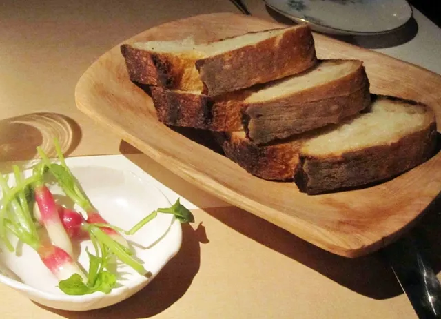 A small woven basket holding slices of rustic bread and a dish of radishes for dipping in olive oil