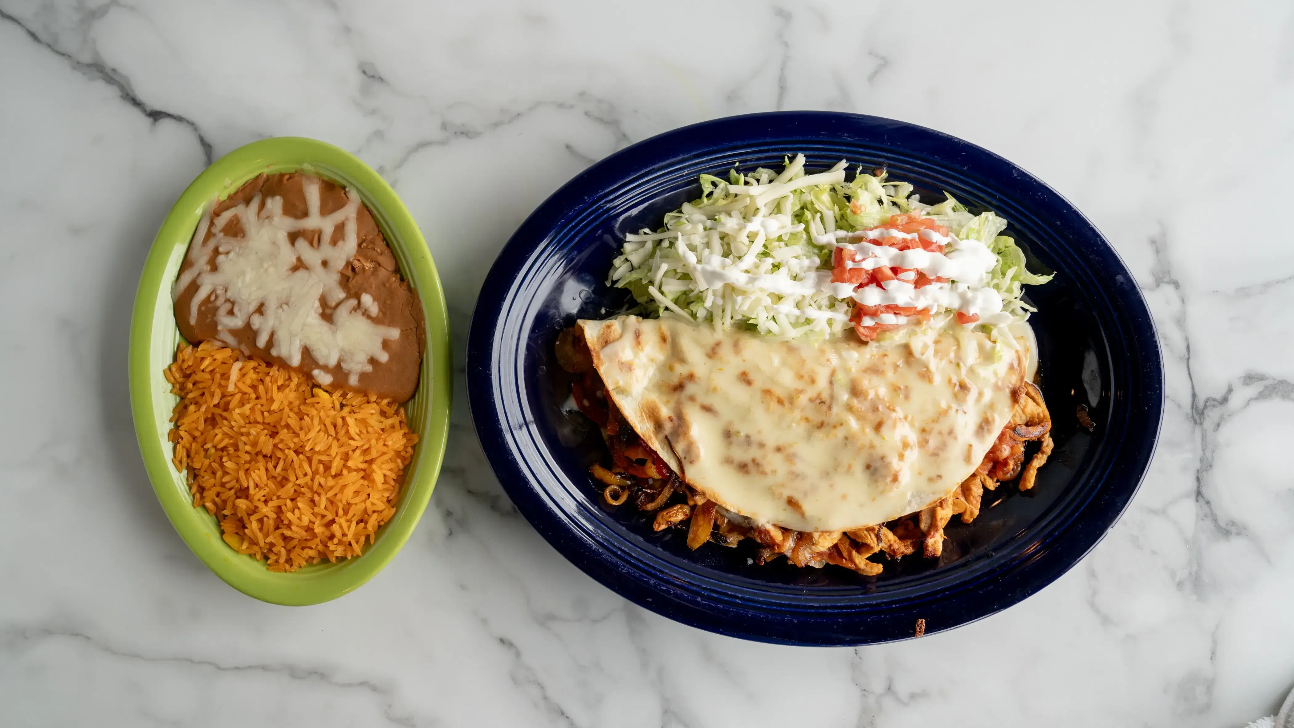 Quesadillas de fajita - Grilled quesadilla filled with your choice of protein, bell peppers, onions, tomatoes, and cheese, covered with cheese sauce. Served with lettuce, sour cream, tomatoes, refried beans, and Mexican rice