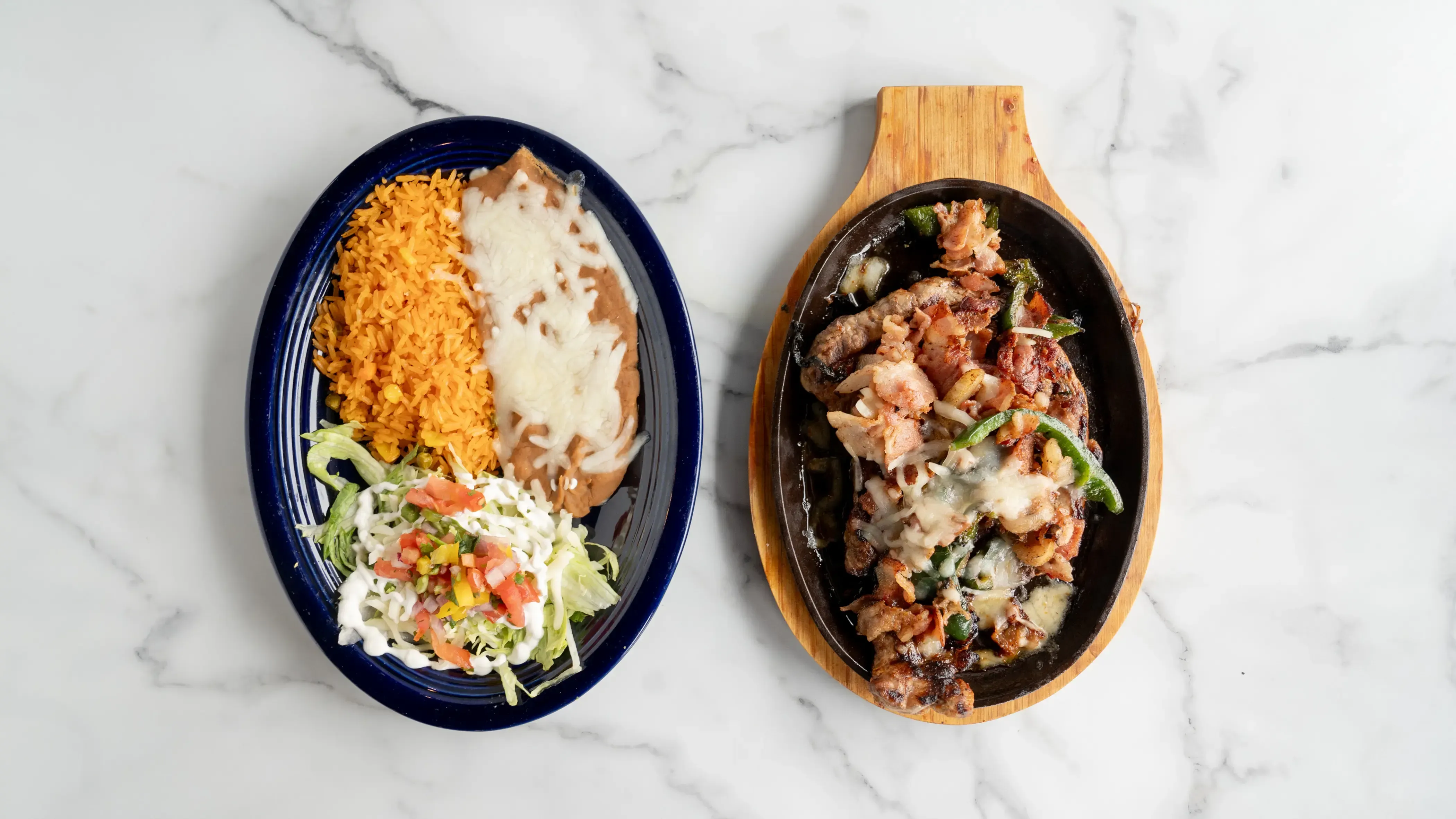 Steak oaxaca - Ribeye steak cooked with crispy bacon and poblano peppers, topped with melted cheese. Served with Mexican rice, refried beans, lettuce, sour cream, tomatoes, and three tortillas