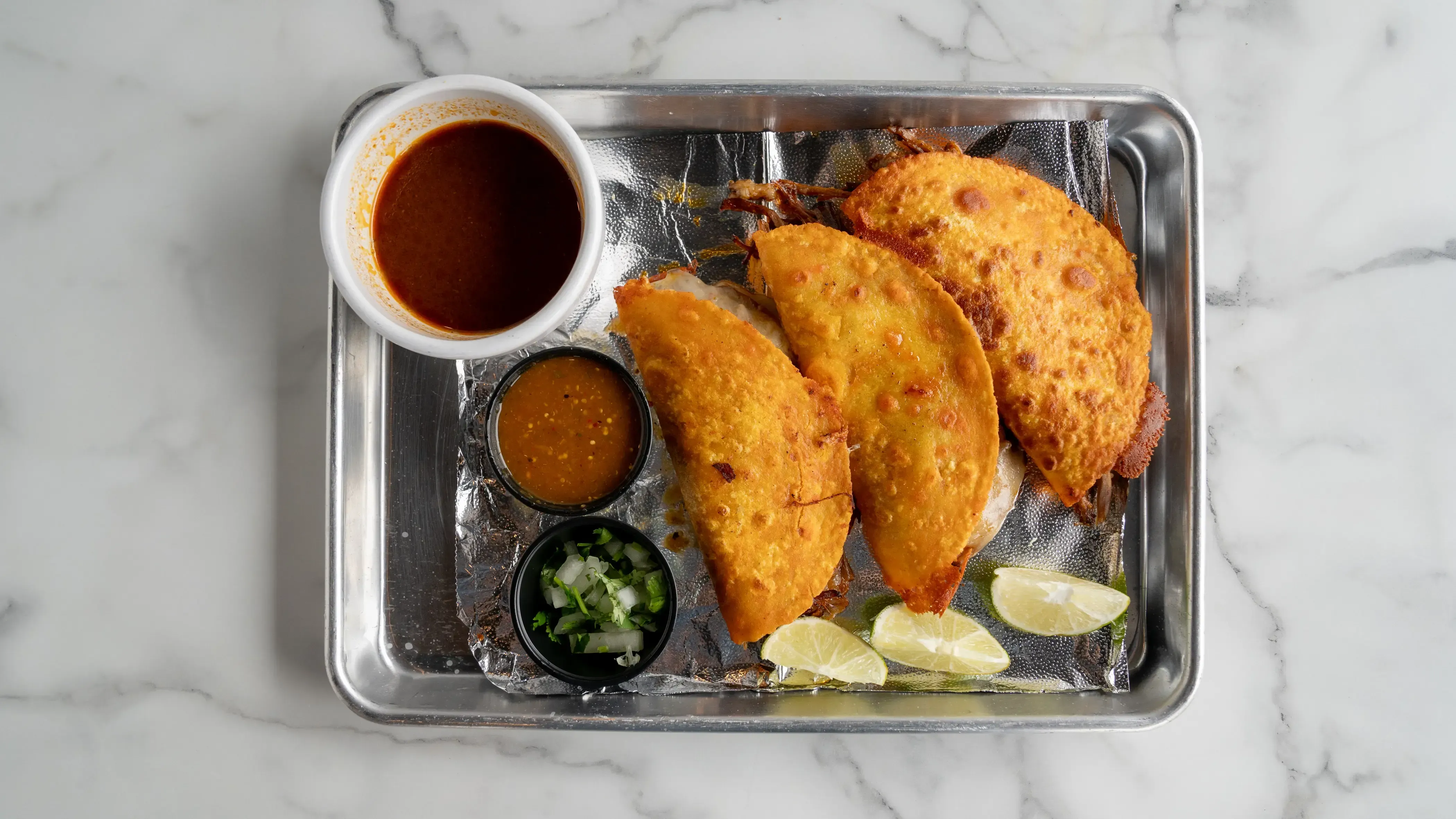 Tacos de birria - Three soft corn tortillas filled with slow-braised birria beef. Served with rich consomé broth for dipping, cilantro, onions, lime, and homemade spicy sauce