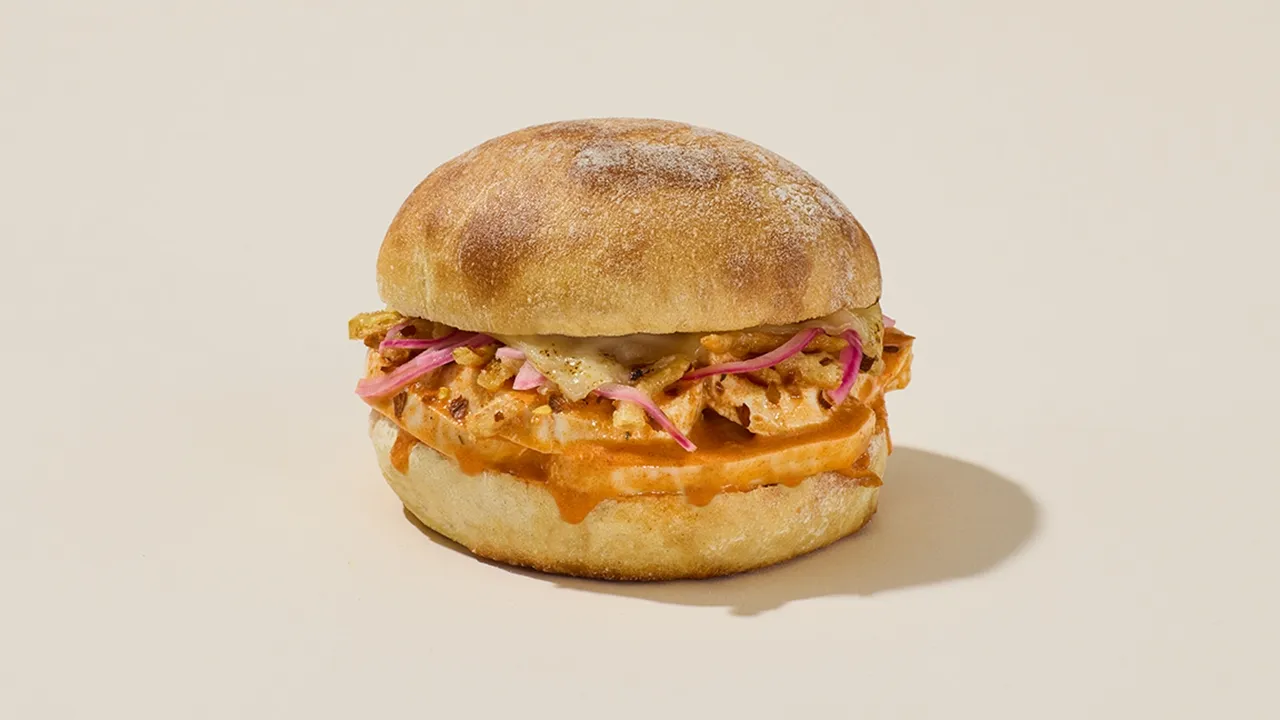 A Pret a Manger Buffalo Chicken Melt sandwich, featuring the in-house made chili crisp that provides a unique 'pop of spice, savoriness, and crunch' to the umami restaurant menu item